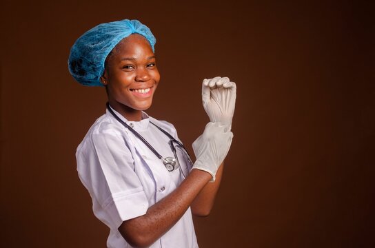 Smiling Nigerian female medic putting gloves on her hands on a brown background