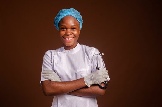 Smiling Nigerian female medic with arms crossed isolated on a brown background