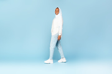Naklejka premium Happy african american woman in hijab walking and smiling at camera over blue studio background, full length shot