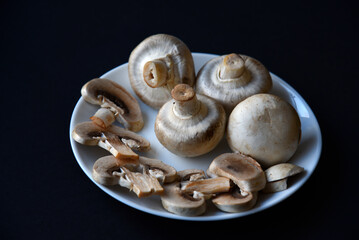 Porcini mushrooms in a white plate on a black background. Fruits of large white champignons close-up. Beautiful mushrooms in a plate.
