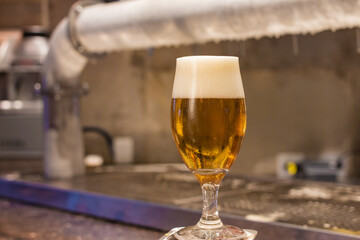 glass of cold and creamy beer on the counter of a lighted bar