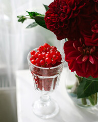 Red currant in a transparent glass next to red flowers