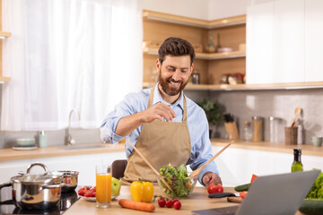 Obraz premium Happy adult caucasian male with beard in apron has video call, making video for meal blog, salting salad