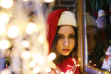 Young attractive girl wearing warm pajamas and a bedspread near the New Year tree. Christmas atmosphere.