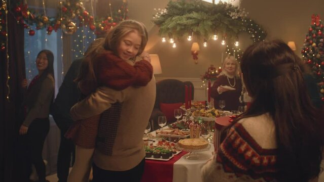 Happy diverse family arriving for dinner party celebrating Christmas or New Year. They hugging, talking, smiling, setting table with dishes. Family holidays and Christmas Eve. Decorations.