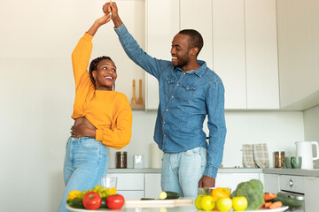 Joyful african american couple cooking and having fun, dancing and spending time in modern kitchen...