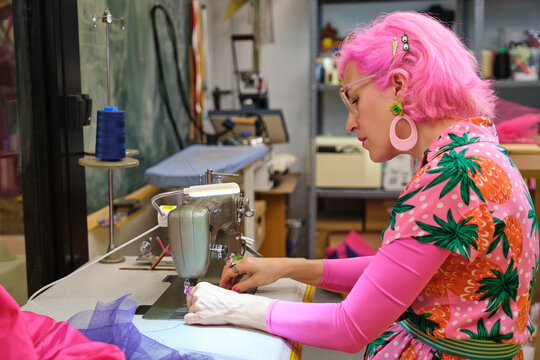 Tailor with pink hair and colorfull clothes threading sewing machine in a sewing workshop.