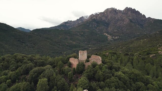 Aerial view circling Castellu di Seravalle, an 11th century military fortress built in the 11th century with the Asco mountains and les Aiguilles de Popolasca in the distance