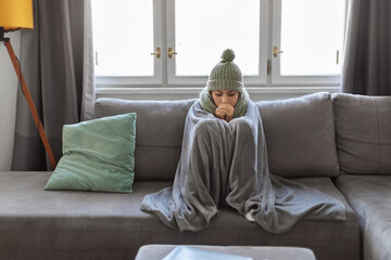 Arab female suffering cold at home, sitting on couch covered with blanket