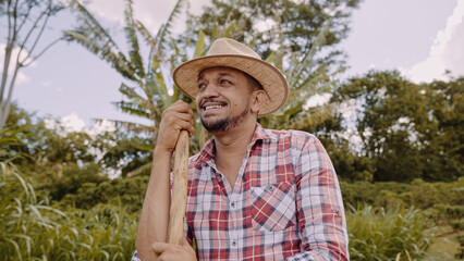 Portrait of young man in the casual shirt holding his hoe in the farm. Farm tool. Latin man.