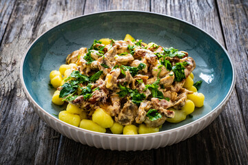 Fried pork loin in creamy sauce with gnocchi and mushrooms on wooden table
