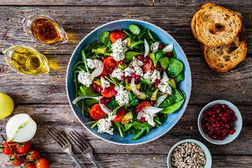 Fresh vegetable salad with feta cheese and pomegranate on wooden table
