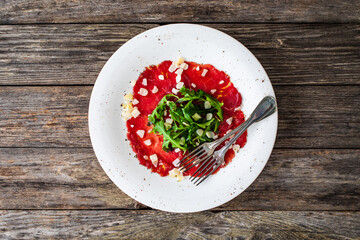 Beef carpaccio with parmesan and arugula on wooden table
