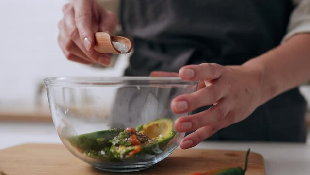 Cook girl salting with a scoop cooked additives, Process cooking for vegetarians green sauce additive stuffing in salad dishes, Salt on a wooden scoop kitchen utensils
