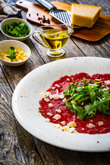 Beef carpaccio with parmesan and arugula on wooden table
