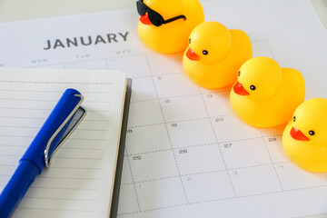 Four yellow rubber ducks in a line on top of January calendar along with notebook and blue pen....