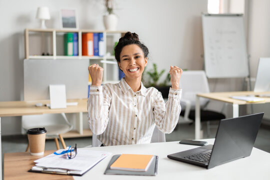 Business luck. Overjoyed female entrepreneur using laptop and shaking fists in joy, celebrating great news, sitting in office