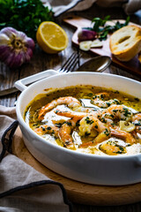 Roast prawns in butter sauce with lemon, garlic and parsley on wooden table
