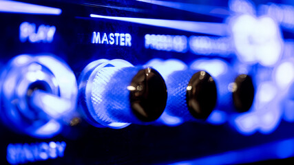 Master toggle switch audio sound level knob detail on music amplifier control panel blue neon light