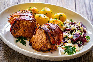 Medium well done pork loin wrapped in bacon with fried potatoes and feta cheese on beets on wooden table
