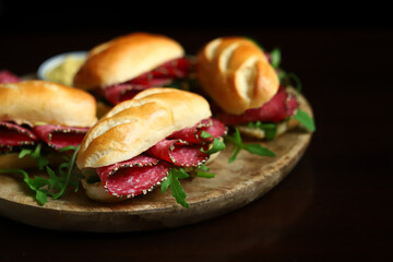 Appetizing salami sandwiches with arugula and mustard on a wooden board.