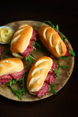 Appetizing salami sandwiches with arugula and mustard on a wooden board.