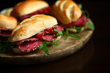 Appetizing salami sandwiches with arugula and mustard on a wooden board.