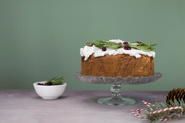 Christmas cake with rosemarry and red berries on a stand on a gray and green background.