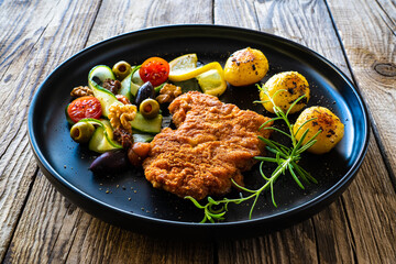 Breaded fried pork chop with fried potatoes and greens on wooden table
