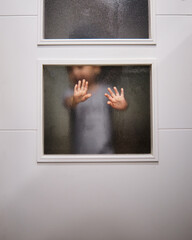 Toddler putting his hand behind a glass door at home, demanding his parent's attention