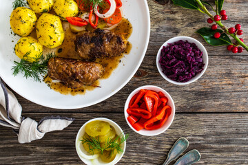 Wrapped pork in sauce served with boiled potatoes and vegetable salad on wooden table
