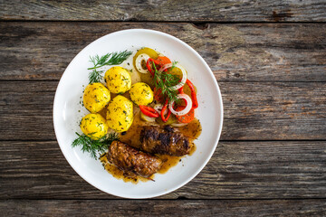 Wrapped pork in sauce served with boiled potatoes and vegetable salad on wooden table
