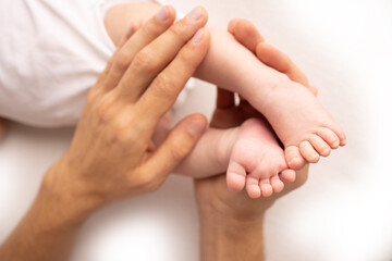 Obraz na płótnie Canvas Children's foot in the hands of mother, father, parents. Feet of a tiny newborn close up. Little baby legs. Mom and her child. Happy family concept. Beautiful concept image of motherhood stock photo. 