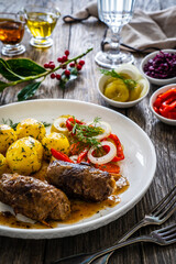 Wrapped pork in sauce served with boiled potatoes and vegetable salad on wooden table
