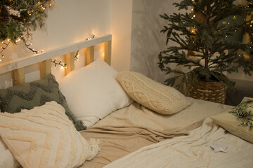 Cozy eco-style bedroom decorated for Christmas. a bed with pillows and blankets near a green Christmas tree with garlands and white toys in a bright spacious room