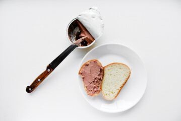 Meat pate and bread with a knife. Spreading pate with a knife on bread on a white background.
