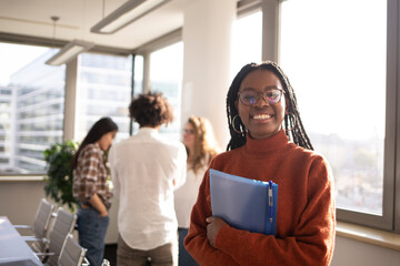 Black girl in office in foreground is looking at camera