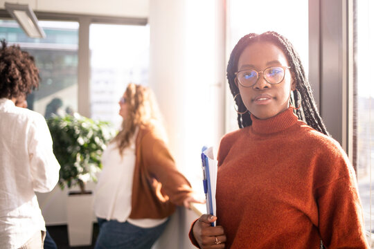 Black girl in office in foreground is looking at camera