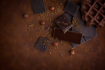 Composition of bars and pieces of different milk and dark chocolate, grated cocoa brown background top view