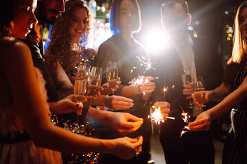 Sparkling sparklers in the hands of friends.Group of people holding sparklers at party. Winter...