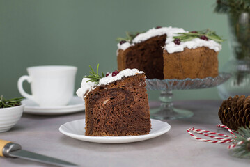 A piece of Christmas cake on plate on grey table with cup of tea and christmas cake on the glass stand.