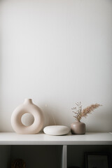 Cozy home interior decor, aromatic candles in glass glowingon white and grey background with natural oil, selective focus of fluffy bunny tail grass, brown jar, lotus flower candle, round matt ceramic