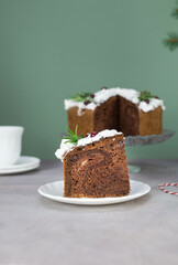 A piece of Christmas cake on plate on grey table with cup of tea and christmas cake on the glass stand.