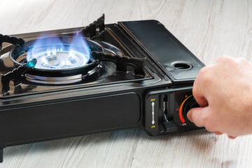 A man's hand turns on a portable gas stove on a wooden table. An alternative source for cooking at...
