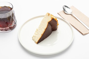 Isolated shot of a plate of sliced San Sebastian cheesecake with a drink and spoon on the side