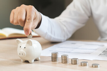 Close up hand of asian young businessman, male putting coin into a piggy ceramic for saving cost,...