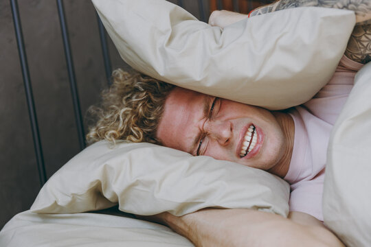 Close Up Young Man Wear White T-shirt Pajama He Lying In Bed Cover Ears With Pillow From Neighbours Noise Snoring Rest Relax Spend Time In Bedroom Home In Own Room Hotel Wake Up. Real Estate Concept.