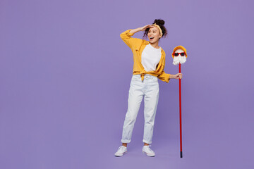 Full body young housekeeper woman wear yellow shirt tidy up hold in hand mop with hat and glasses hold head at forehead look aside isolated on plain pastel light purple background Housework concept