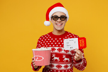 Young smiling man in red knitted Christmas sweater Santa hat posing 3d glasses watch movie film...
