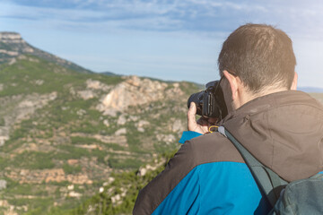 Man with backpack and slr camera takes photos to the landscape in the morning